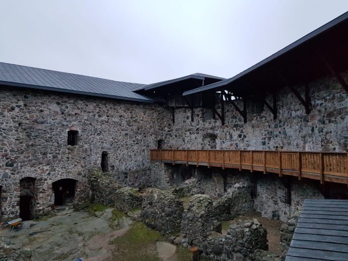 Yleisnäkymä sisäpihalta, jossa uudet puurakenteet ja katto kiertävät muureja